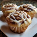 Three Golden Swirl Cinnamon Roll Cupcakes topped with icing on a white plate, a cozy treat.