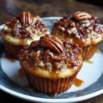 Three Gooey Pecan Pie Cupcakes on a plate, topped with pecans and caramel drizzle.