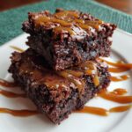 Two Gooey Salted Caramel Brownies stacked on a white plate with caramel drizzle.