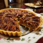 A slice of Ultimate Gooey Southern Pecan Pie being lifted from the pie on a floral patterned plate.