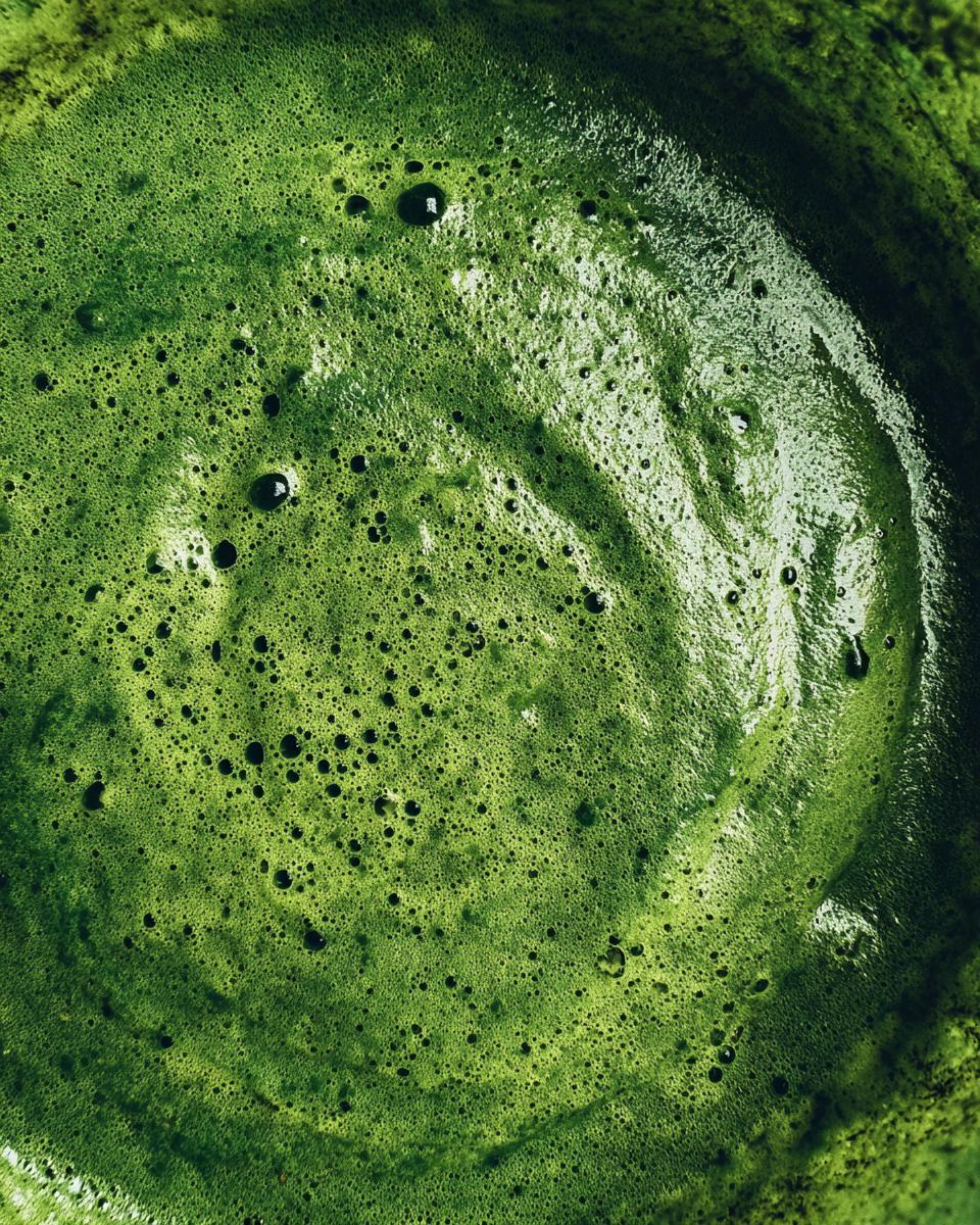 A top-down view of a vibrant green detox smoothie, showcasing its smooth texture and tiny bubbles.