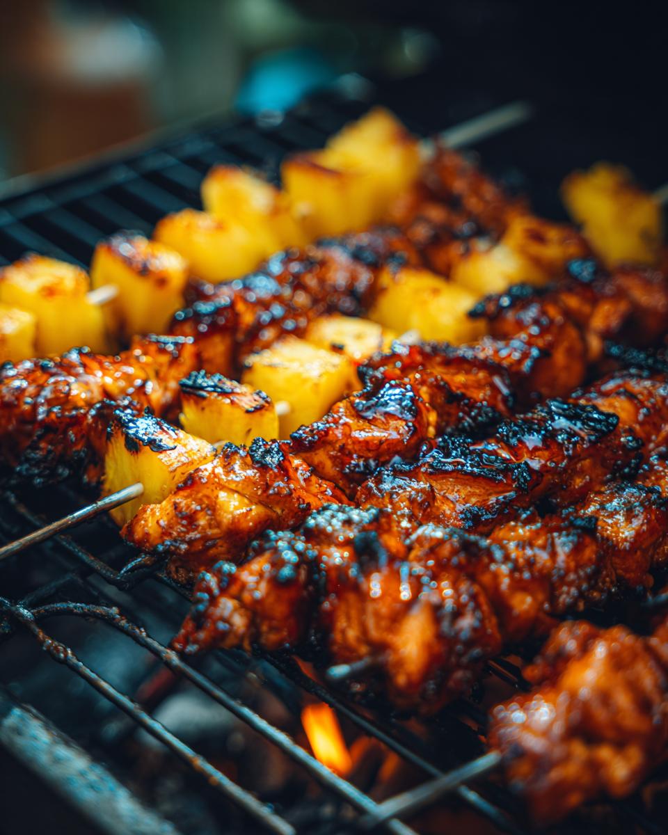 Close-up of Grilled Pineapple Chicken Skewers cooking on a grill with flames visible underneath.