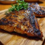 Two grilled swordfish steaks on a wooden board, garnished with fresh herbs. Ready to serve.