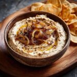 Wooden bowl filled with Homemade Caramelized Onion Dip, topped with caramelized onions and served with pita chips.
