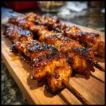 Close-up of juicy 4-ingredient honey garlic chicken skewers on a wooden board, glistening with sauce.