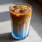 A refreshing The Iced Blueberry Latte in a glass with ice, showing the layered blue and coffee colors.