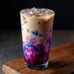 A refreshing The Iced Blueberry Latte in a glass with ice, blueberry swirls, and a creamy coffee layer.