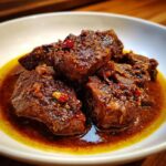 Close-up of Fall-Off-The-Bone Jamaican Brown Stew Chicken in a white bowl, showcasing the rich, flavorful sauce.