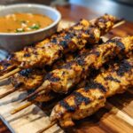 Grilled Juicy Secret! Best Chicken Satay Skewers on a wooden board with a side of peanut sauce.