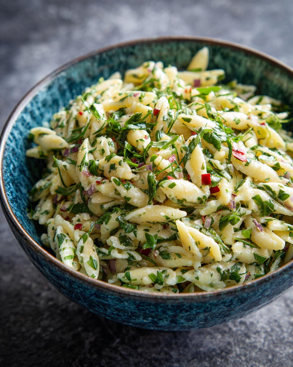 Close-up of Lemon Basil Pasta Salad in a blue bowl, featuring pasta, fresh basil, and red onion.