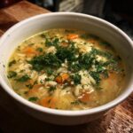A bowl of Bright & Cozy Lemon Chicken Orzo Soup, garnished with fresh herbs and visible carrots.
