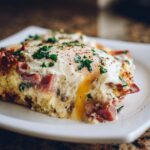 Close-up of a slice of Make-Ahead Eggs Benedict Casserole with a runny yolk and garnished with parsley.