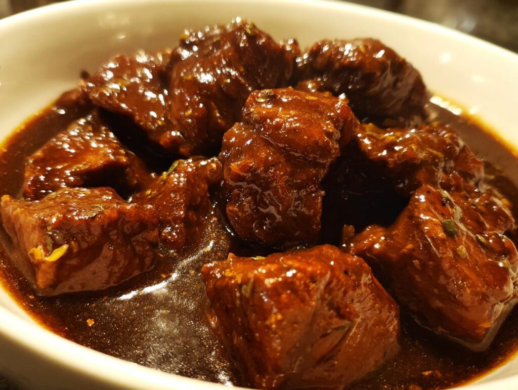 Close-up of tender Melt-in-Your-Mouth Crockpot Beef Tips in a rich, dark gravy, served in a white bowl.