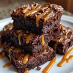 A stack of decadent Miso Caramel Brownies drizzled with caramel and sprinkled with chocolate chips.