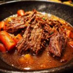 Close-up of Mississippi Pot Roast in a bowl, featuring tender shredded beef, carrots, and rich gravy.