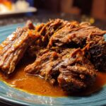 Close-up of tender Mississippi Pot Roast served on a blue plate with rich gravy.