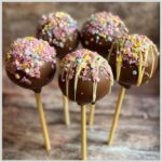Five no-bake cake pops covered in chocolate, sprinkles, and drizzled with white chocolate.