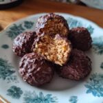 A plate of 15-Min No Bake Chocolate Rice Krispie Balls, one cut in half to show the inside texture.