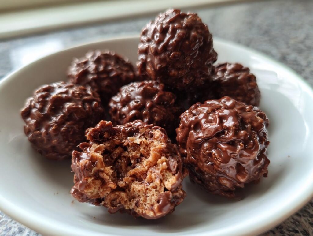 A plate of delicious 15-Min No Bake Chocolate Rice Krispie Balls, one broken open to show the inside.