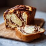 A sliced loaf of No-Yeast Amish Cinnamon Bread on a wooden board, showcasing the cinnamon swirl.