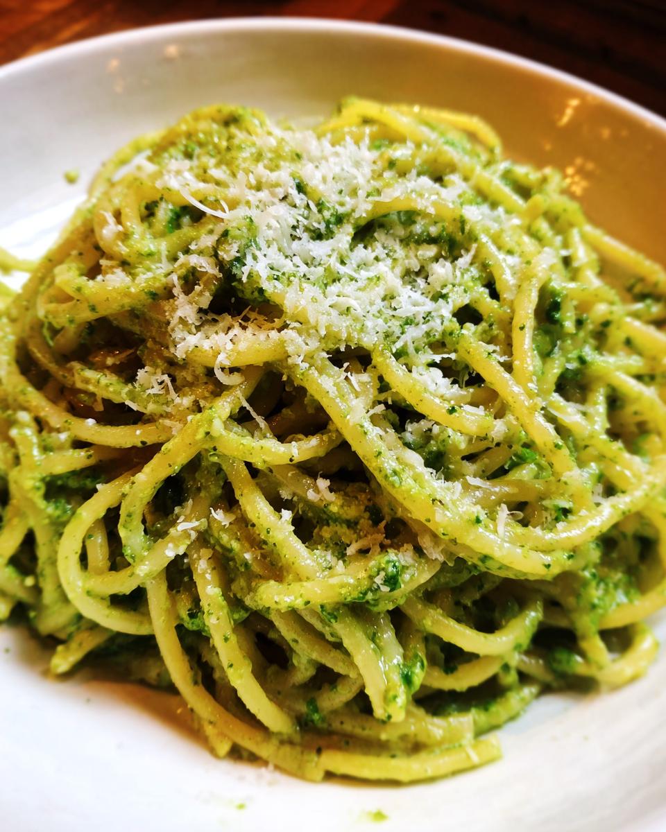 Close-up of One-Pot Creamy Pesto Pasta, topped with grated Parmesan cheese, served on a white plate.