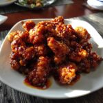 A plate of glistening Orange Chicken, coated in a sweet and savory sauce and sprinkled with sesame seeds.