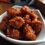 Close-up of flavorful Orange Chicken pieces in a white bowl, coated in a glossy sauce.