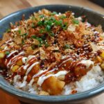 A delicious Packed Street Corn Chicken Rice Bowl in a gray bowl, topped with sauces and garnishes.