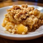 Close-up of a delicious Peach Crumble dessert in a white bowl, showcasing the golden peaches and crumbly topping.