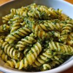Close-up of a bowl of pesto pasta salad, featuring spiral pasta coated in vibrant green pesto sauce.