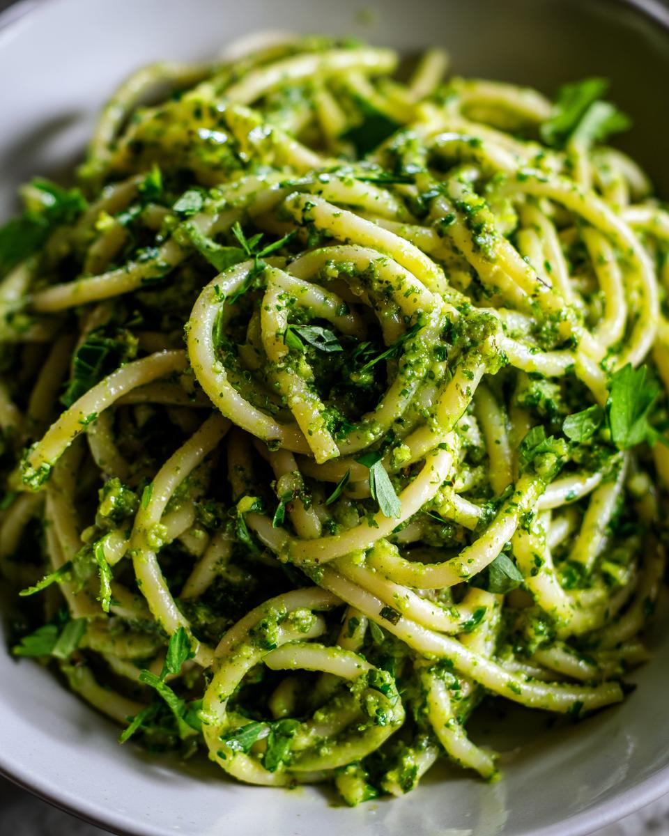 Close-up of a bowl of vibrant green Pesto Pasta Salad, garnished with fresh herbs.
