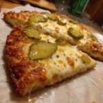 Close-up of two slices of Pickle Pizza Viral Salty Slice, topped with melted cheese and sliced pickles.