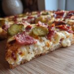 Close-up of a Pickle Pizza Viral Salty Slice with pickles, cheese, and meat toppings on a wooden board.