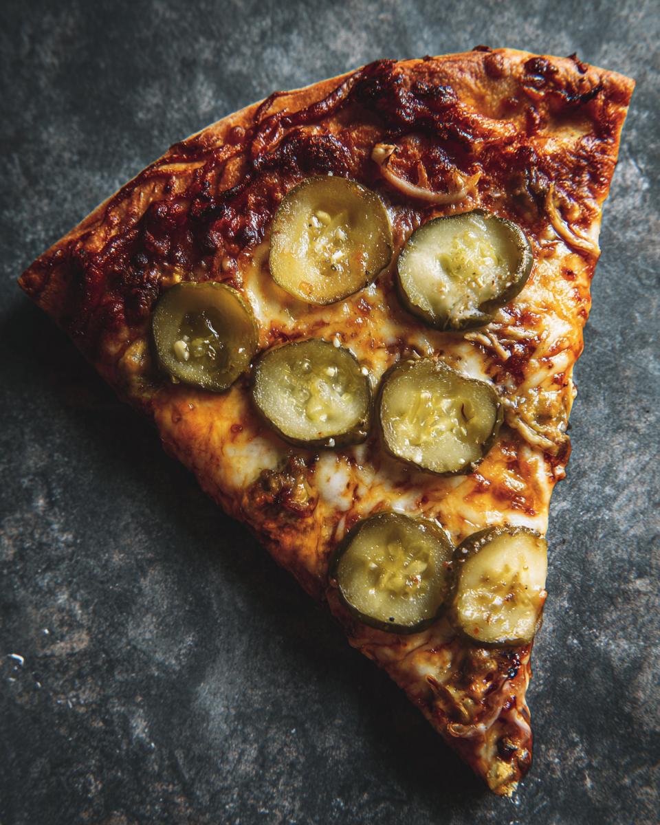 A slice of Pickle Pizza Viral Salty Slice with pickle toppings on a cheesy base.