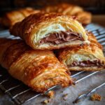 A stack of golden brown 20-Minute Puff Pastry Chocolate Croissants, one cut open to show the chocolate filling.