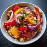 A vibrant Quinoa Summer Bowl featuring quinoa, red onion, and colorful bell peppers, garnished with fresh herbs.