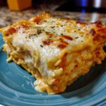 A slice of Ramen Lasagna on a blue plate, showcasing layers of ramen noodles, sauce, and melted cheese.