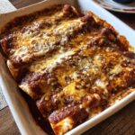 A baking dish filled with Restaurant-Style Red Cheese Enchiladas, topped with melted cheese and red sauce.