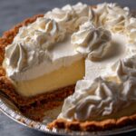 A whole Silky Smooth Banana Cream Pie with a slice removed, showing the layers of crust, filling, and whipped cream.