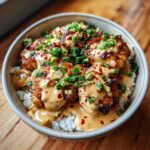 Bowl of Smothered Chicken Rice, topped with creamy sauce, green onions, and red pepper flakes.