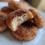 A close-up of Soft & Chewy Churro Cookies, one with a bite taken out, showing the soft interior and cinnamon-sugar coating.