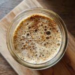 Overhead view of an active sourdough starter in a glass jar, showing bubbles. Master Your Sourdough Starter now!