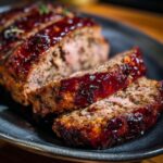 Slices of juicy Stove Top Stuffing Meatloaf with a glazed topping on a dark plate.