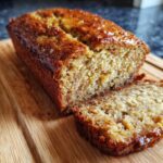 A loaf of Ultimate Moist Sugar-Free Banana Bread with a slice cut, sitting on a wooden board.