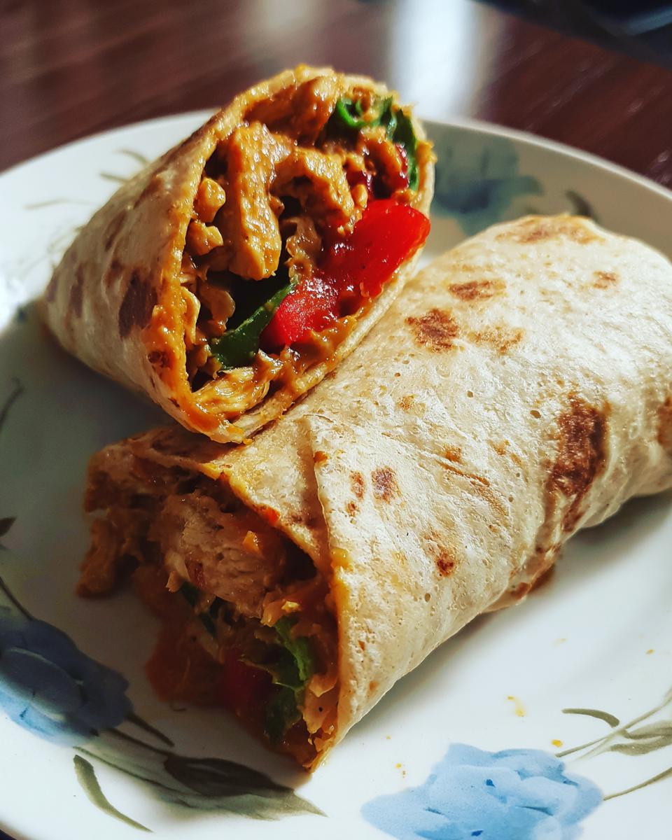 Two halves of a 30-Minute Thai Peanut Chicken Wraps on a decorative plate, showcasing the filling.
