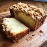 A slice of Ultra Moist Sour Cream Coffee Cake with crumb topping on a wooden board.