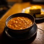 A bowl of Vegan Tomato White Bean Stew, served with cornbread on a rustic wooden table.