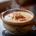 Close-up of steaming, velvety cream of crab soup in a decorative bowl, topped with crab meat.