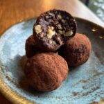 Close-up of Viral No-Bake Dubai Chocolate Balls dusted with cocoa powder, one cut in half to show the inside.