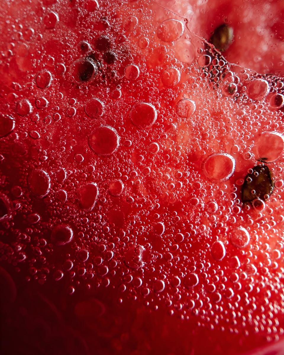 Macro shot of The Watermelon Juice with bubbles, showcasing its vibrant red color and refreshing texture.